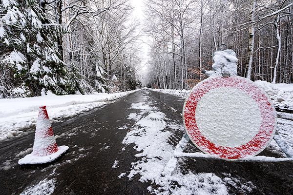 Symbolfoto einer verschneiten Straße mit einem Straßenhütchen und einem Einfahrt-Verboten-Verkehrsschild