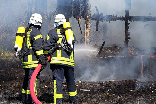 Zwei Freiwillige der Feuerwehr löschen einen Brand mit einem Schlauch
