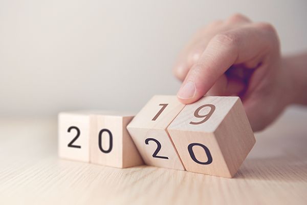 Symbolfoto: Vier Holzwürfel mit Zahlen, eine Hand dreht zwei Würfel um die gezeigte Zahl von 2019 auf 2020 zu ändern