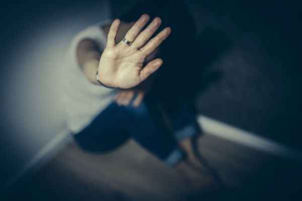 Symbolbild Gewalt: Eine Person sitzt in der Ecke eines Zimmers am Boden und streckt die Hände abwehrend in die Höhe